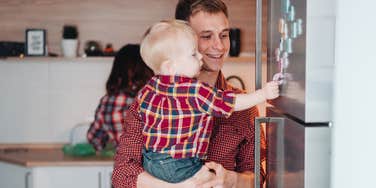father holding son touching the fridge at home