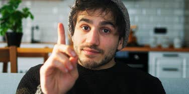 Man raises a finger mid-conversation, the polite "may I jump in" moment before speaking up.