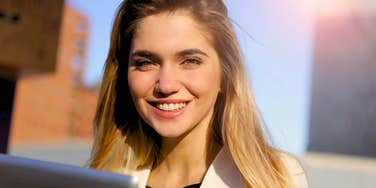 intelligent woman smiling outside with her laptop