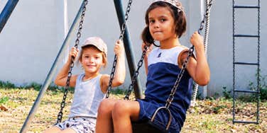 Two kids swing on the kind of chain-link swing set every Gen X childhood seemed to have.