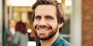 Man with a beard gives a broad, genuine smile outdoors.