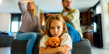 sad scared little girl holding teddy bear while parents argue
