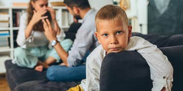 young boy sitting with parents bickering behind him