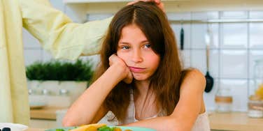 sad little girl sitting next to overbearing mother