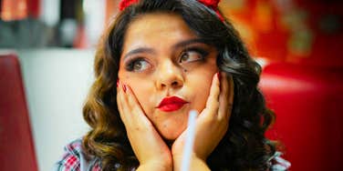 Woman in a retro diner setting gazes upward in thought, piecing together a memory from years working there.