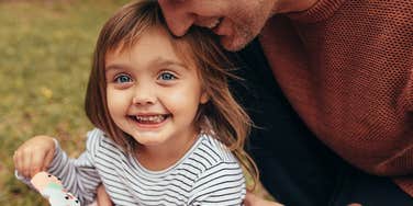 Dependable dad hugging his smiling young daughter outdoors