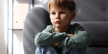 boy whose parents are condescending looking sad by a couch