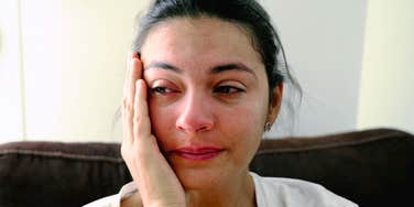 Woman crying quietly, resting head on hand, reflecting the exhaustion of caregiving
