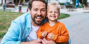 a dad who is deeply loved by his young son smiles and laughs next to him 