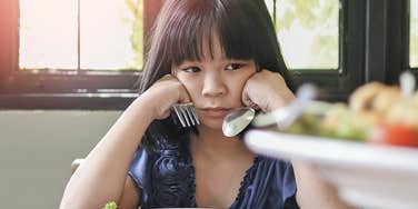 little girl whose parents lack boundaries looks sad at the dinner table