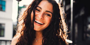 Woman smiling genuinely in sunlight, embodying simple joyful habits of people who enjoy life fully