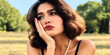 Woman rests her chin on her hand, gazing off in thought, weighing whether to let someone back in.