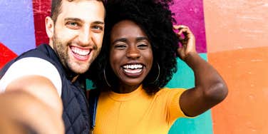Joyful man and woman smiling brightly and feeling like a million bucks by a colorful wall