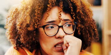 Woman bites her nails, brow furrowed, the visible worry behind insisting she's fine.