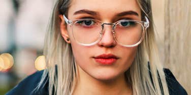 Woman with glasses gives a direct, serious look toward the camera.