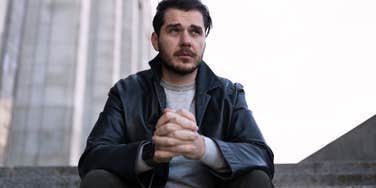 Serious man sitting on steps outside in a city looking defeated