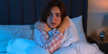 grown woman scared in her bed listening to creepy sounds