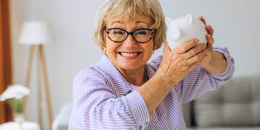 frugal older woman holding piggy bank smiling