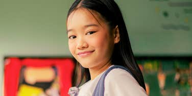Student in a classroom smiling in a uniform with a backpack.