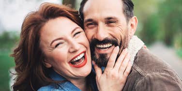 We are happy together. Joyful husband and wife are bonding to each other with fondness. They are looking at camera and laughing while standing on path outdoor