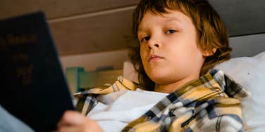 child reading a book in bed alone feeling unheard by parents