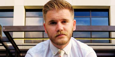 Man in white shirt and floral tie looking directly at camera with a serious expression.
