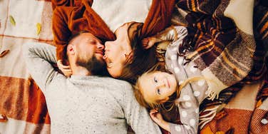 silly kid smiling on an autumn blanket with her parents in love