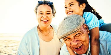 loving older parents playing with their child on the beach at sunset