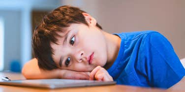 boy eating dinner while watching his tablet and looking sad 
