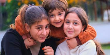 three siblings smiling together hugging