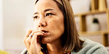 Woman with shoulder-length brown hair biting her fingernail and gazing off-camera with a worried expression.