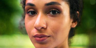 Close-up of a woman with dark curly hair and brown eyes looking calmly at the camera against a green blurred background