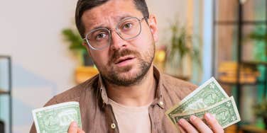 man holding dollar bills and looking frustrated 