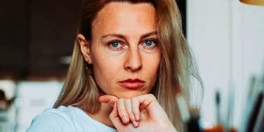 Woman with long blonde hair, serious guarded expression.