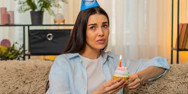 awkward woman holding a birthday cupcake about to be sung to