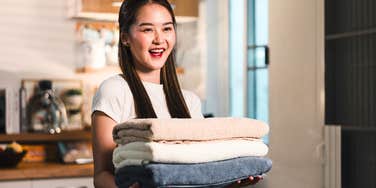 Gen Z woman holding folded towels while cleaning house