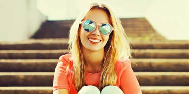 blonde woman in sunglasses sitting on steps, smiling