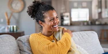 A Black woman with hair in a ponytail smiles in a sunny room