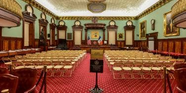 empty room where the NYC city council usually meets, filled with empty chairs and empty dais