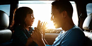 Asian father playing with his daughter in a car, boy laughing, backlit