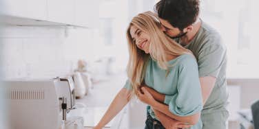 Bearded guy standing behind attractive blonde girl and kissing her. They are waiting for hot drink