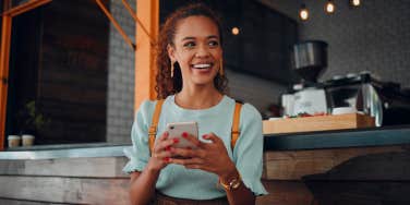 happy woman sitting at coffee shop holding phone