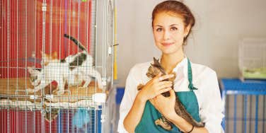 animal shelter working holding cats next to kennel of cats