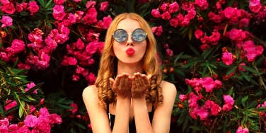 woman blowing kiss in front of pink flower bushes