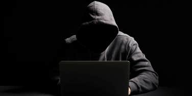 anonymous man sitting in the dark on his computer