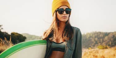 blonde woman in beanie carrying a surfboard
