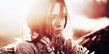 woman looking sad holding flowers, sun behind her head