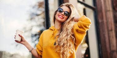 blonde woman smiling and wearing sunglasses while touching her hair