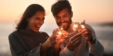 woman and man lighting sparklers on beach