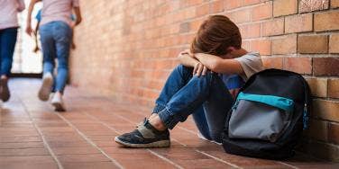 upset kid sitting against wall with his backpack